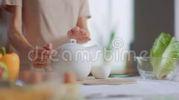 女人从茶壶里把茶倒进杯子里女士在家准备早餐茶视频的预览图