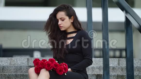 穿着紧身衣的女人坐在街上拿着花在楼梯上扔红玫瑰的女人视频的预览图