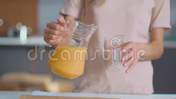 女人往厨房的玻璃杯里倒果汁喝橙汁的女士视频的预览图