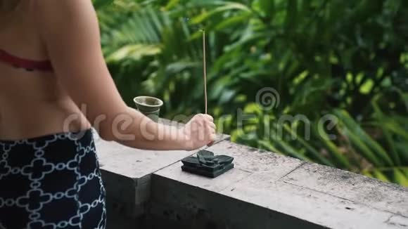女人的手紧紧地放着芳香的棍子背景上有绿色植物视频的预览图