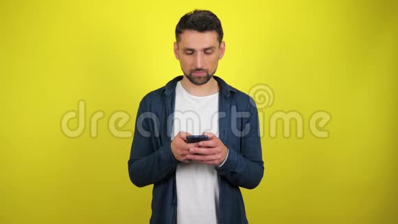 一个穿着蓝色衬衫和白色T恤的年轻人很感兴趣地使用智能手机视频的预览图