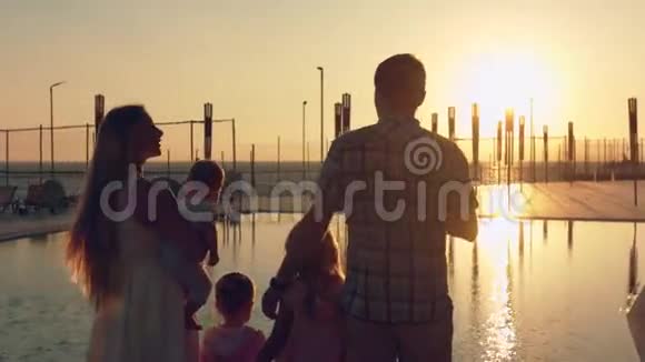 幸福的家庭有三个孩子在欣赏游泳池表面的日落视频的预览图