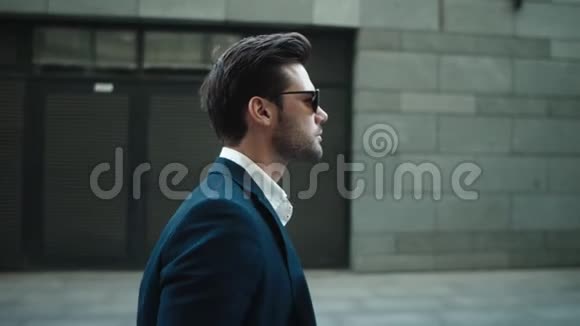 侧视商人穿西装走路街上戴太阳镜的男人视频的预览图