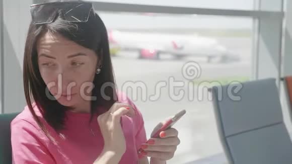 一个年轻漂亮的女孩坐在机场候车室用手机女人买电子机票做酒店视频的预览图