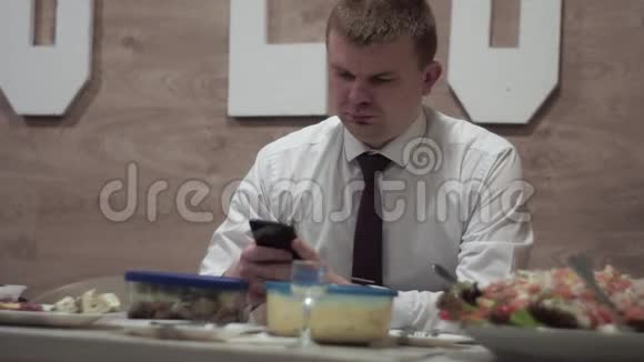 一个度假的人坐在一张有食物的桌子旁看着一部智能手机视频的预览图