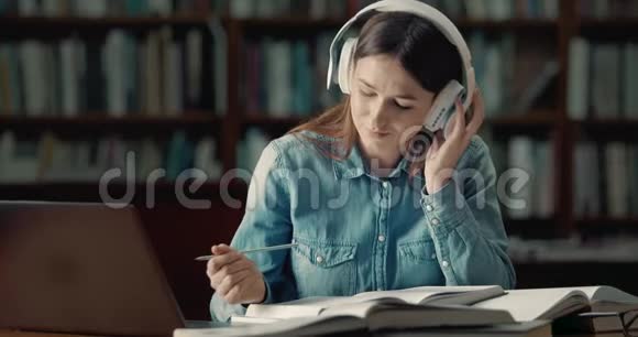 在图书馆读耳机的女学生视频的预览图
