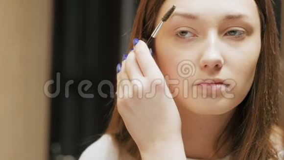 女孩用刷子梳眉毛年轻女人在脸上化妆照镜子女性美的概念视频的预览图