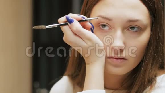 美丽的黑发女孩用刷子画眉毛轮廓年轻的女人在脸上化妆在美的倒影中看着视频的预览图