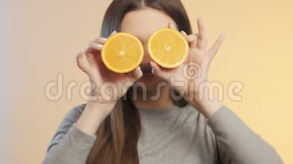 可爱的女孩脸上带着一半的橘子水果做鬼脸十几岁的孩子在演播室背景上玩得开心心情积极自负视频的预览图