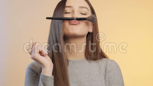 有趣的女孩做鬼脸在彩色的画室背景上用化妆刷到处胡闹年轻的女人心情积极女性视频的预览图