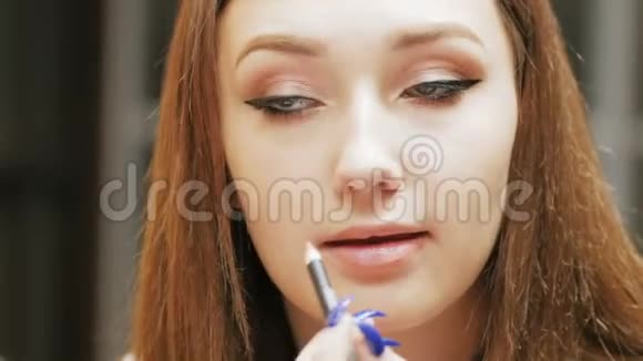 自信的黑发女孩用一支化妆铅笔画着嘴唇的轮廓年轻的女人在化妆时看着镜子里的美视频的预览图