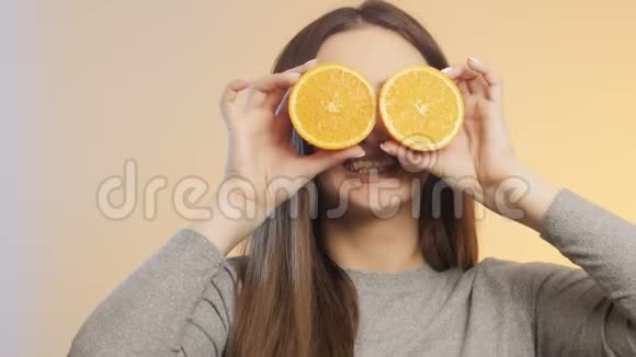 可爱的女孩脸上带着一半的橘子水果做鬼脸十几岁的孩子在演播室背景上玩得开心心情积极自负视频的预览图