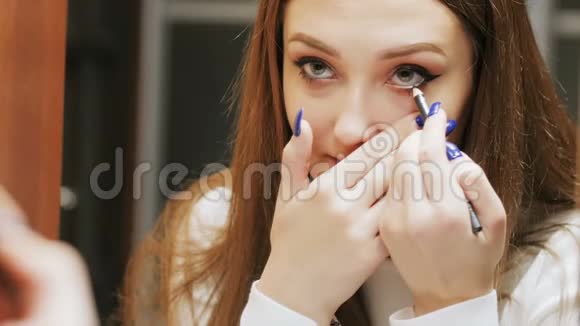 美丽的黑发女孩用一支化妆铅笔画了一个眼睛轮廓年轻的女人正在化妆在美的倒影中寻找视频的预览图