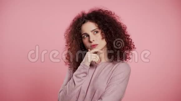 思考女人在粉红色的背景上抬头看了看担心沉思的面部表情漂亮的卷发模特视频的预览图