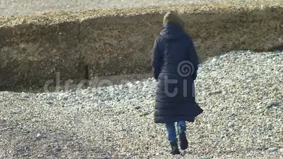 穿外套的女人走在鹅卵石海滩上复制空间视频的预览图