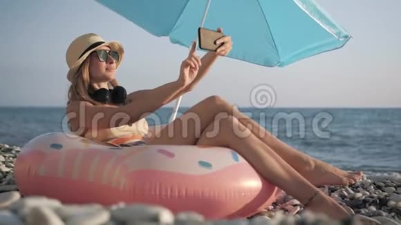 美丽的女孩在海滩上用智能手机自拍视频的预览图