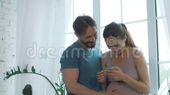 特写喜孕夫妇看手机在家视频的预览图