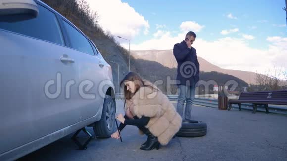 幽默女人换了一个汽车轮子有人在打电话视频的预览图
