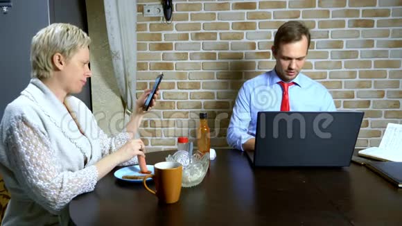一个男人在家里用厨房里的笔记本电脑工作妻子吃视频的预览图