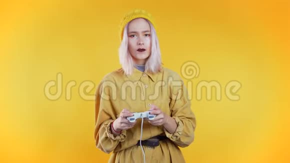 漂亮的年轻女孩在TV上玩电子游戏黄色的工作室墙上有操纵杆利用现代技术视频的预览图