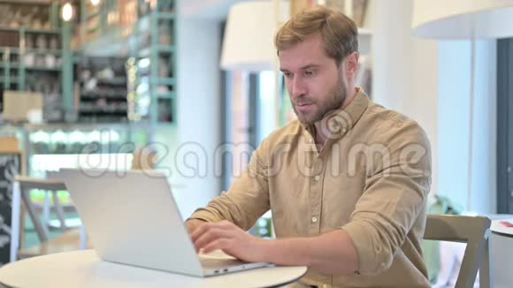 青年男子在咖啡厅镜头前微笑使用笔记本电脑视频的预览图