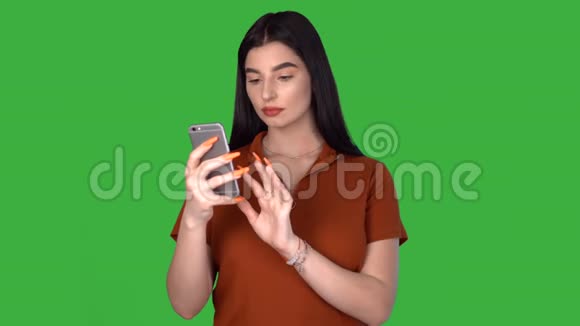 年轻女性在绿色屏幕上用移动应用程序发短信微笑着享受视频的预览图