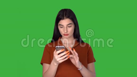 年轻女子拿着手机发短信笑着使用手机应用程序绿色屏幕视频的预览图