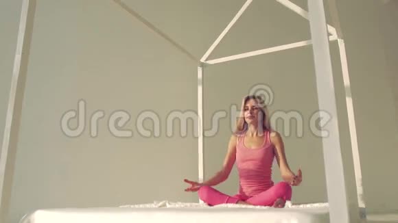 年轻的瑜伽女人穿着粉红色的运动布在床上做瑜伽视频的预览图