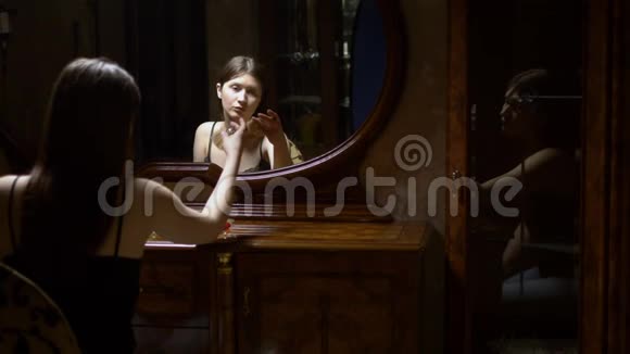 美丽的女孩戴上耳环黄昏时坐在镜子前视频的预览图