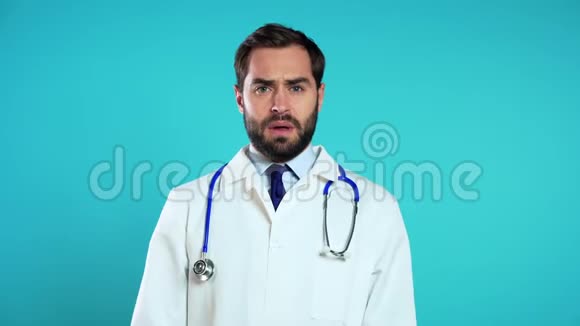 穿着职业医疗白大褂的疲惫医生的肖像被隔离在蓝色上视频的预览图