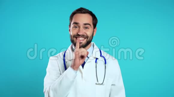 戴着医用外套的医生微笑的画像手指在蓝色的嘴唇上视频的预览图