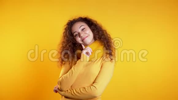 年轻漂亮的卷发女孩站在黄色的画室背景上调情视频的预览图