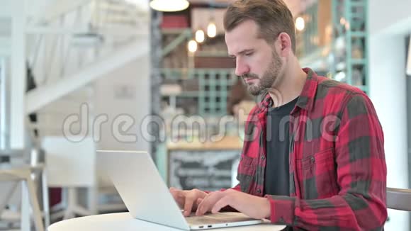 疲劳的颈部疼痛的年轻人在咖啡厅用笔记本电脑视频的预览图