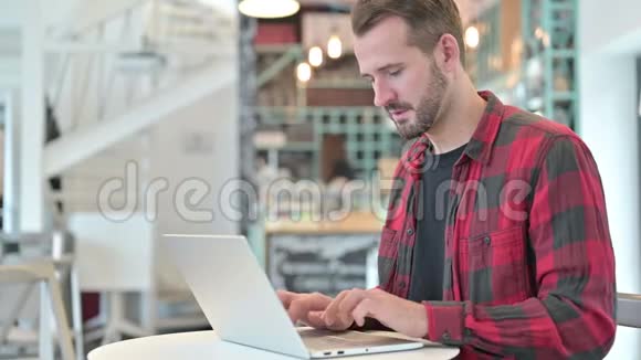 在咖啡厅用手提电脑咳嗽的年轻人视频的预览图