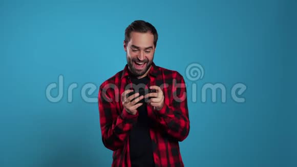 帅哥在蓝色工作室墙上的智能手机上玩游戏使用现代技术应用程序社交网络视频的预览图