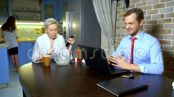 一个男人在家里用厨房里的笔记本电脑工作妻子吃视频的预览图