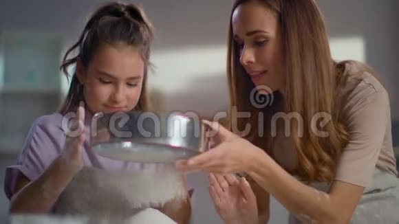 快乐的母亲帮助女儿在厨房里用筛子筛面粉视频的预览图