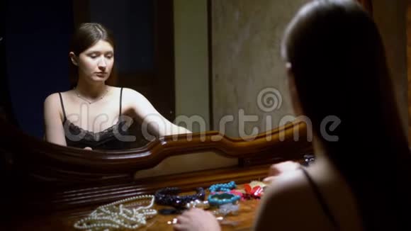 黄昏时分美丽的女孩坐在镜子前看着她的珠宝视频的预览图