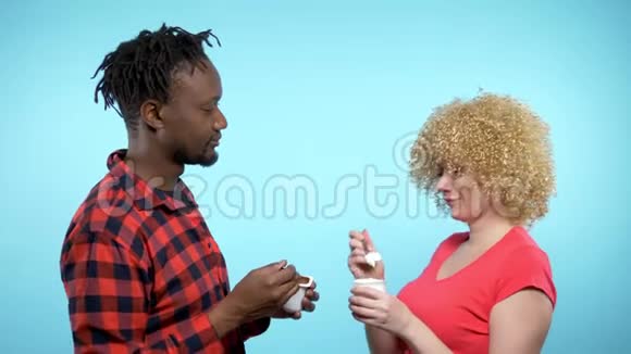 非洲男人白种人女人吃巧克力和奶油酸奶蓝色背景视频的预览图