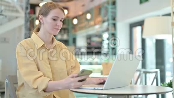 有手提电脑的年轻女子在咖啡厅里讲智能电话视频的预览图