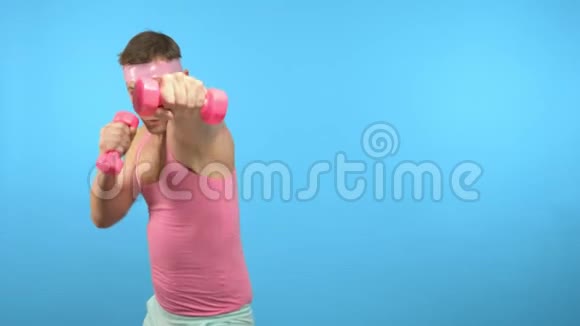 穿着粉红色衬衫的英俊男子正在与粉红色哑铃进行健身视频的预览图
