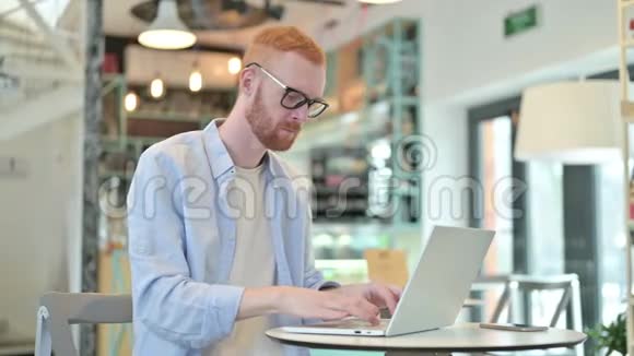 红发男子颈部疼痛用笔记本电脑在咖啡厅视频的预览图