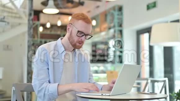 红发男子在咖啡厅使用笔记本电脑震惊表情视频的预览图