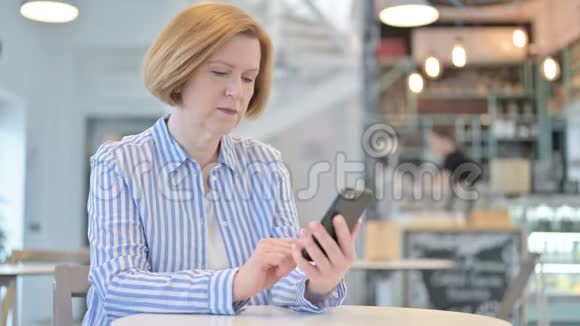 创意老女人在咖啡厅使用智能手机视频的预览图
