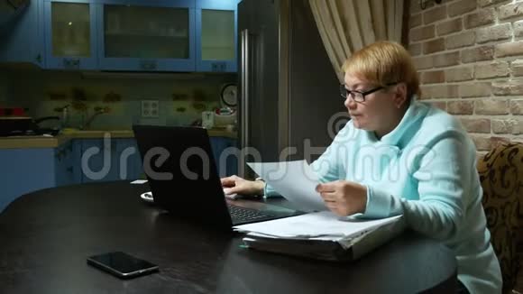 使用笔记本电脑在家拿文件的老年妇女视频的预览图