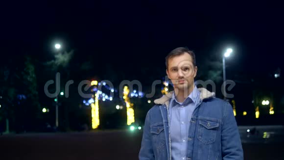 一个穿夹克衫的帅哥晚上在一条城市街上看着摄像机视频的预览图
