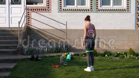 年轻的运动女性在家户外用橡皮筋做深蹲运动视频的预览图