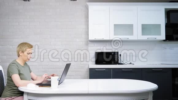 一个女人用笔记本电脑坐在厨房的桌子上她很高兴视频的预览图