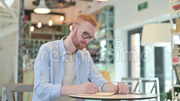 严肃的红发男子在咖啡厅做文书工作视频的预览图