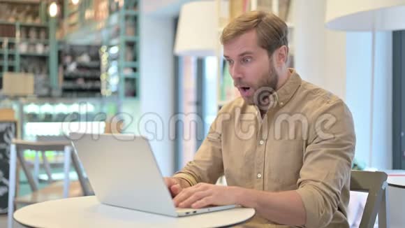 青年男子在咖啡厅手提电脑庆祝成功视频的预览图